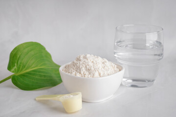 Scoop and bowl with collagen powder and glass of water on white background