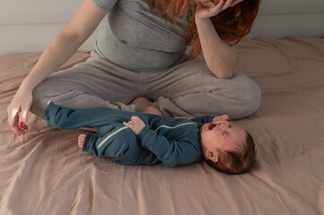 A Caucasian woman sits on a bed next to a crying baby. Postpartum depression.