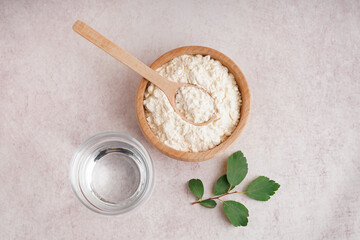 Glass of water, wooden bowl and scoop with collagen powder on beige grunge background