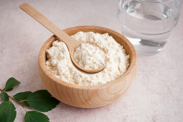 Glass of water, wooden bowl and scoop with collagen powder on beige grunge background