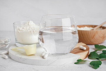 Glass of water, pills, bowl and scoop with collagen powder on white background