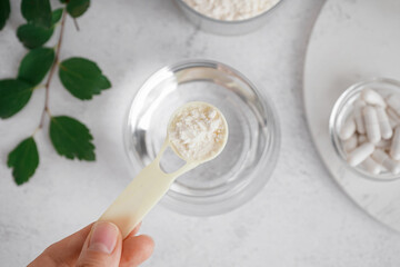 Female hand adding collagen powder into glass on white background