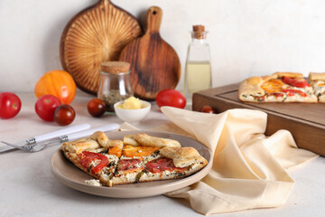 Plate with pieces of tasty tomato galette on white background