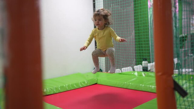 A young girl jumping on a trampoline. Child, girl, jumping, trampoline, playroom, kid, play, happy. Happy kid playing in a lifestyle playroom. Describe.