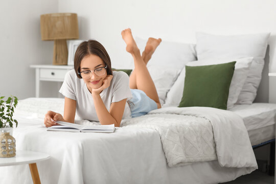 Beautiful young happy woman reading book on bed at home
