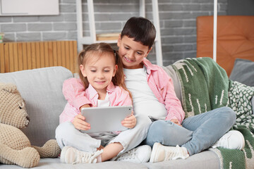 Cute happy little kids with mobile phone and tablet playing video games on sofa at home