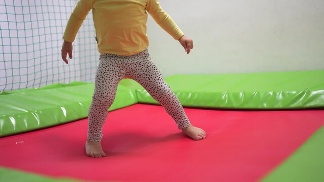 A young girl jumping on a trampoline. Child, girl, jumping, trampoline, playroom, kid, play, happy. Lifestyle happy kid playing in a playroom. Describe.