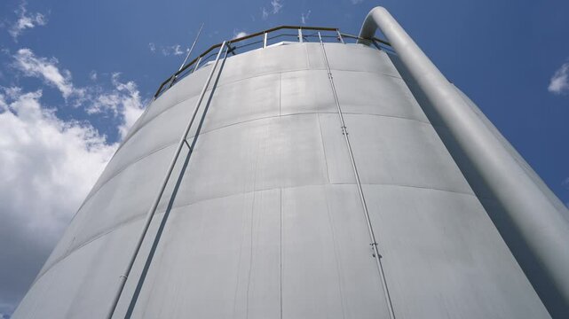 A large oil storage tank against a blue sky. Storage, processing, chemical industry equipment. Tank the vertical steel. Lightning protection device on tanks. Production of petroleum products
