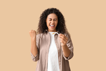 Young African-American woman with broken cigarette celebrating success on beige background. Stop...