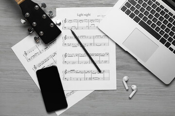 Music sheets with laptop, mobile phone, earphones and guitar on grey wooden background