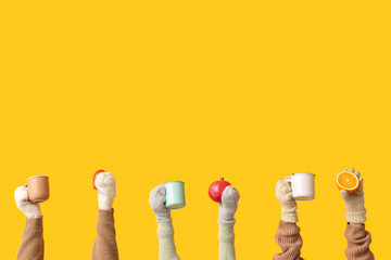Female hands in mittens holding fruits and mugs of tasty mulled wine on yellow background