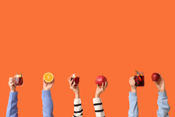 Female hands with fruits and glasses of tasty mulled wine on orange background