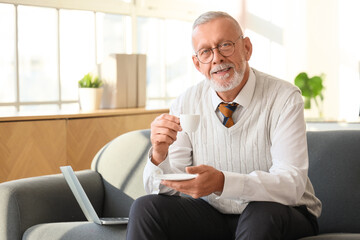 Senior businessman with cup of coffee sitting on sofa in office