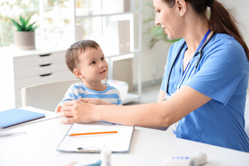 Obraz premium Female pediatrician with cute little boy at table in clinic