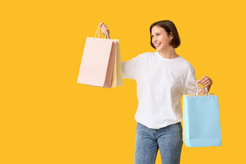 Young woman in blank t-shirt with shopping bags on yellow background