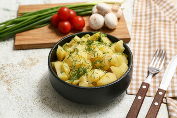 Bowl of tasty potato salad with ingredients and cutlery on light grunge background