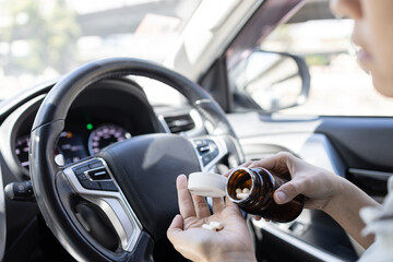 Woman pouring medicine capsule into her palm of hand,taking medication while driving a car,dangers...