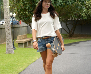 A woman is walking at the city park while carrying a skateboard in her hands