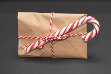 festive gift envelope in thick yellow kraft paper, elegantly tied with a red-and-white ribbon, sits beside a classic Christmas candy cane against a dark background, evoking holiday cheer