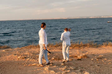 Couple Beach Sunset - Two people stand on a cliff overlooking the ocean at sunset.