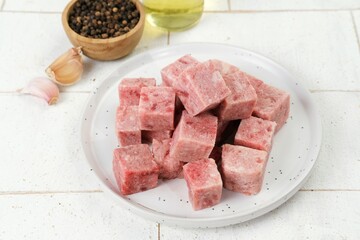 Close-up of saikoro beef cubes, perfectly diced and placed in a white plate. Surrounded by garlic,...