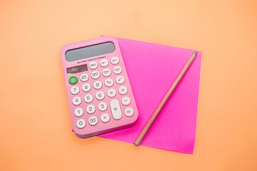 A pink calculator, a pink pencil, and a pink paper on an orange background