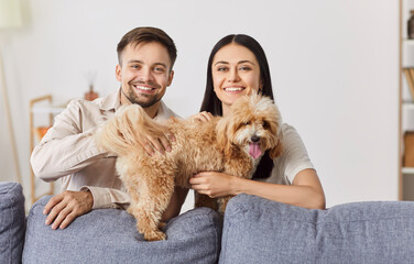Young smiling couple, happy family bonding with cute pet puppy at home, childfree spouses enjoy...