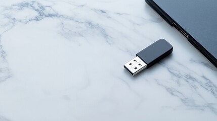 Fototapeta premium Black USB flash drive on marble surface near laptop.