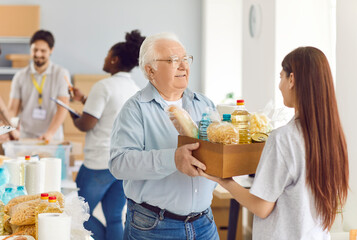 Volunteer gives a box of food to an elderly male pensioner at a social assistance center. The...
