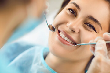 Smiling face of a woman at the dentist, close-up. Beautiful smile of a young woman, dentist tools, shallow focus. Hygiene teeth cleaning in the clinic. Orthodontic services, filling installation