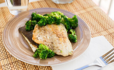 Fried fillet of sea bass with garnish of broccoli on black warm stone plate