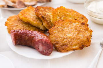 Potato pancakes with fried sausage on white plate