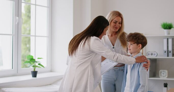 Little boy patient with mother standing at doctor's office in clinic with friendly female pediatrician after medical examination. Child health care and medicine concept. 4k video. Slow motion video.