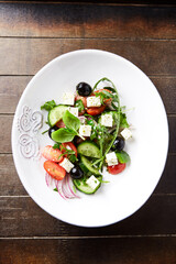 Healthy Salad with Feta Cheese, Black Olives, Cucumber and Cherry Tomatoes. Wooden background. Top view. Close up.	