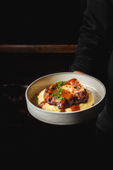 A beautifully plated dish featuring tender meat on a bed of creamy mashed potatoes, garnished with herbs and drizzled with savory sauce. Perfect for culinary and food-themed projects.