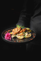 A gourmet dish featuring grilled chicken, lemon slices, and vibrant pink pickled cabbage, artfully presented on a black plate against a dark background. Perfect for food-related themes.