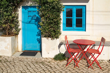 red table with chairs near the white house with a blue door, Portugal