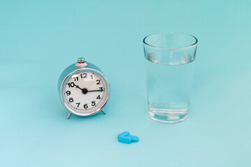 Alarm clock, pills, and glass of water on blue background