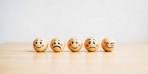 Wooden emoji faces showing happy, sad and neutral emotions on a white background wooden surface.