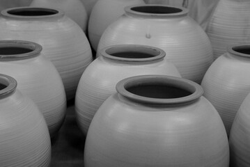 Large unglazed clay jars with smooth surfaces are neatly arranged, reflecting traditional Japanese craftsmanship used for storage and everyday use. Black and white photography.