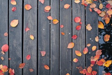 Colorful Autumn Leaves Spread Across a Weathered Wooden Dock Beside Calm Water Creating a Serene and Inviting Fall Atmosphere