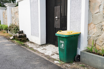 Green trash can on the front fence of the house
