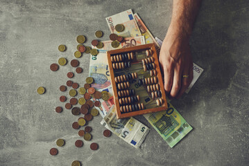 Man counting money on gray table with abacus and euro banknotes