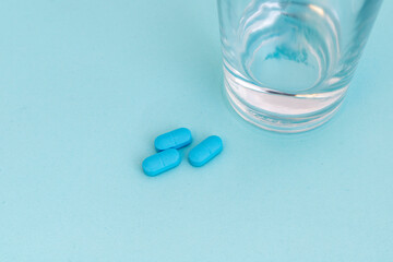 A glass of water with blue pills on blue background