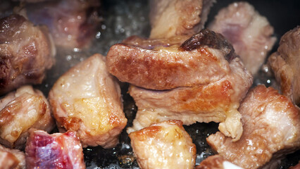Fried pieces of meat close-up, pork from fatty meat at home. Food cooked in a pan. Very bold. Delicious frying of meat products. Cooking in a rustic style, top view. pieces of meat are fried in oil