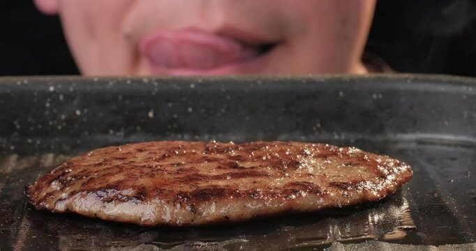 Hungry man watching burger patty grilling on a frying pan isolated on black background. Tasty hamburger or cheeseburger preparation