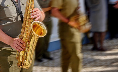 Obraz premium A golden saxophone shines in the sunlight as musicians gather for a lively performance on a cobblestone street in a warm afternoon atmosphere