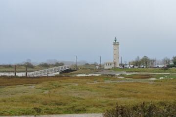 Lighthouse standing tall by the shore on a cloudy day with a wooden pier in the foreground