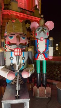 A vertical view of a group of large colorful nutcracker statues, including the Mouse King, displayed outdoors at night as part of the holiday decorations.