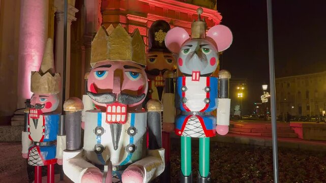 A horizontal view of a group of large colorful nutcracker statues, including the Mouse King, displayed outdoors at night as part of holiday decor.